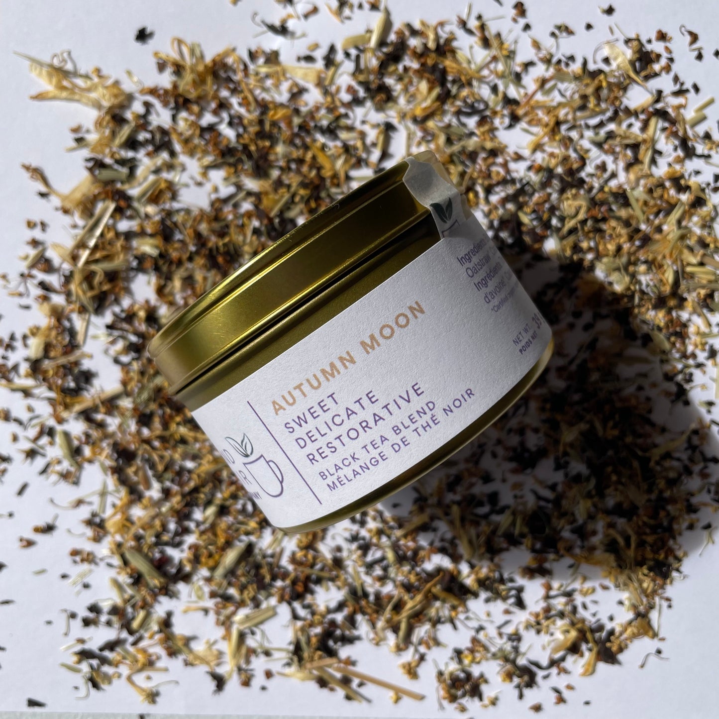 Essential size tin of Autumn Moon black tea blend on a background of scattered tea