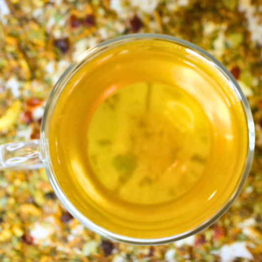 Cinnamon Sunshine Tea Brewed. Herbal tea with lemon and cinnamon steeped in a glass tea cup with scattered loose leaf tea in the background.