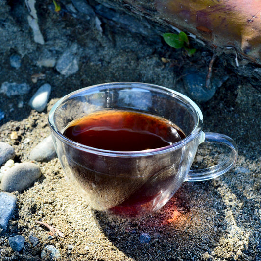 Junior year Pu'erh steeped in glass tea cup on beach near tree