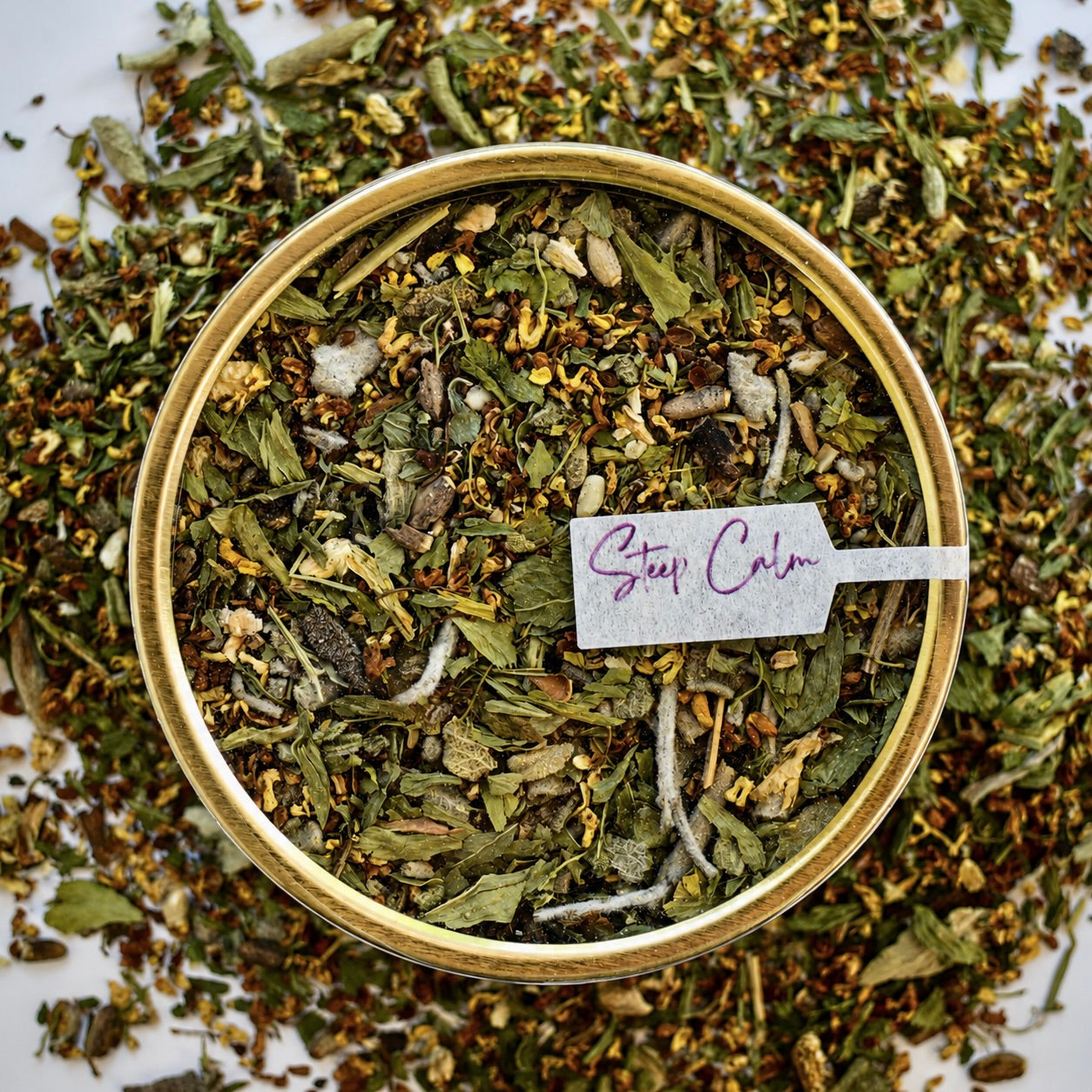 The Legends Herbal Tea 30 cups of tea size gold finish tin sitting on loose tea that contains Milk thistle seed, Osmanthus, Dandelion root, Alfalfa, Sage, Rosemary.