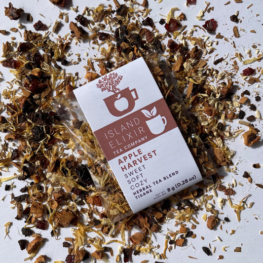 Island Elixir Apple Harvest herbal tea 'Dicsover' size package surrounded by loose tea leaves on a white background