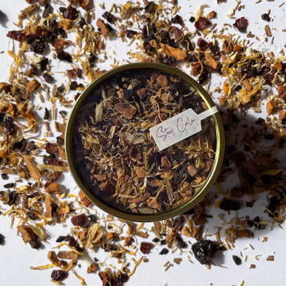 Island Elixir Apple Harvest herbal tea 'Essential Tin' size package viewed from the top and surrounded by loose tea leaves on a white background