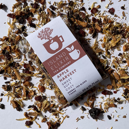 Island Elixir Apple Harvest herbal tea 'Savour' size package surrounded by loose tea leaves on a white background