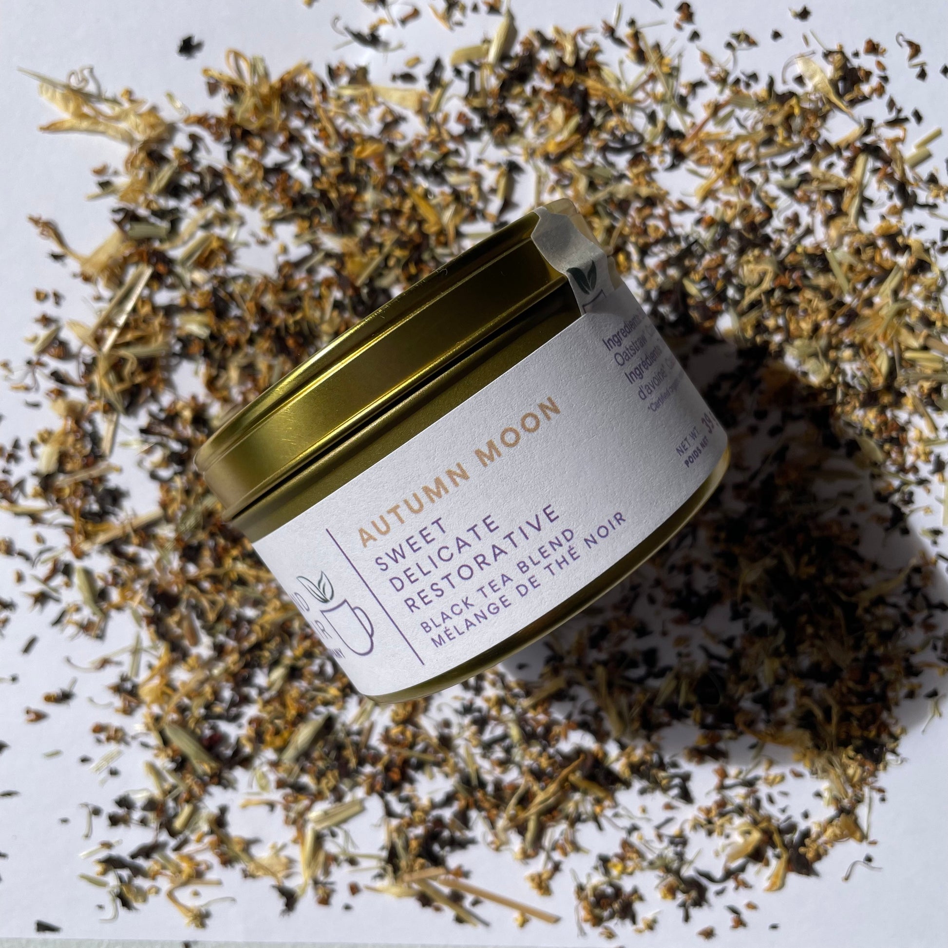 Essential size tin of Autumn Moon black tea blend on a background of scattered tea