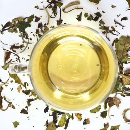 Bai Mu Dan sweet white tea. Tea Steeped in a glass cup surrounded by loose tea leaves.