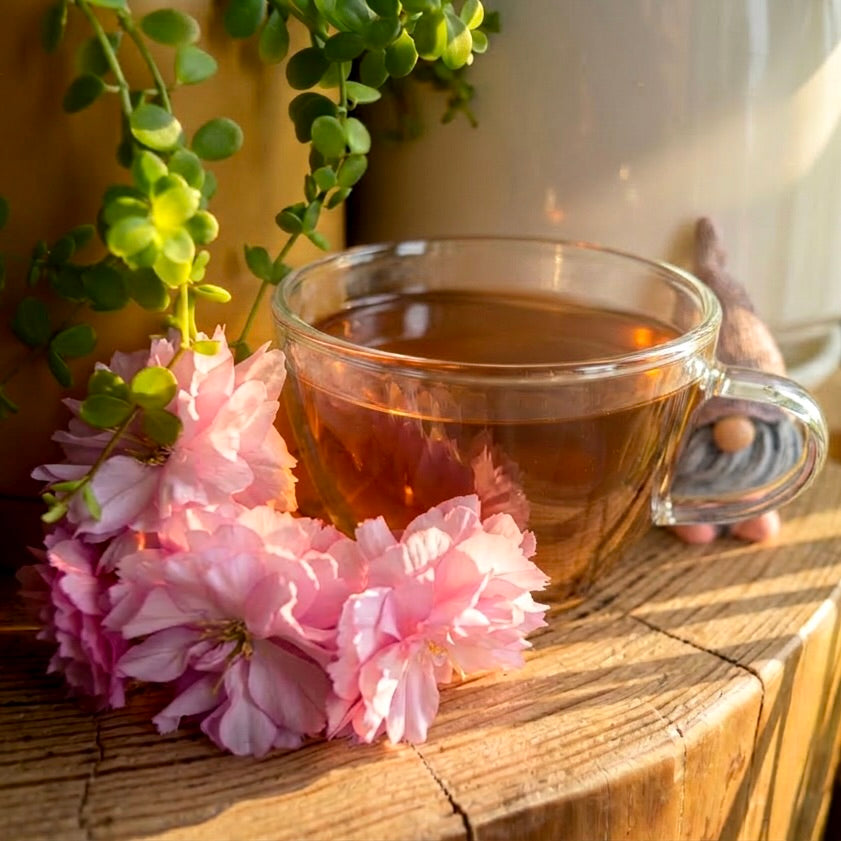 Cherry Grove loose left steeped tea leaves on a log with plants cherry flowers and a small gnome.