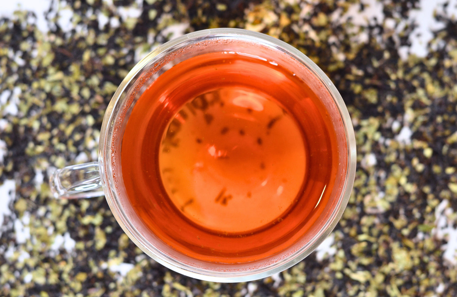 A view looking down on a glass teacup holding perfectly brewed First Light black and Yerba mate tea blend with scattered tea leaves in the background.