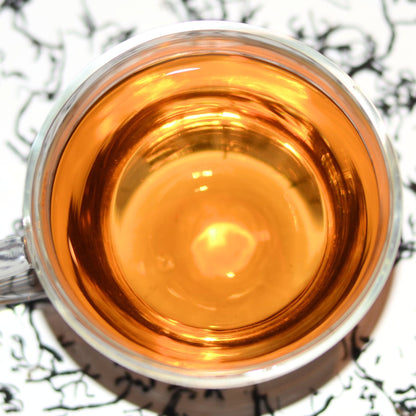 Imperial Keemun Mao Feng Tea Brewed in a glass tea cup. This photo shows the light, honey brown colour of the tea and hints at the flavour of dried pear, chocolate, and orchid.