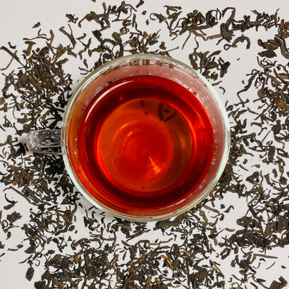 Junior Year Puerh dark tea in a glass cup on  top of scattered tea leaves on a white background