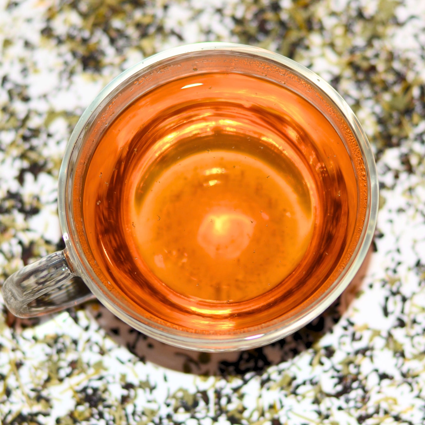 Pacific Forest Tea Brewed to show the amber colour of the tea. In the background, see the blend of loose leaf tea - Douglas Fir needles, Sri Lankan black tea (Ceylon tea), and nettle. A beautiful representation of the essence of Vancouver Island. For 'tea near me' shop loose leaf tea in Langford, BC.