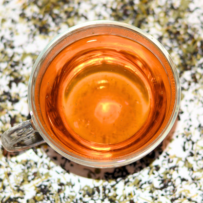Pacific Forest Tea Brewed to show the amber colour of the tea. In the background, see the blend of loose leaf tea - Douglas Fir needles, Sri Lankan black tea (Ceylon tea), and nettle. A beautiful representation of the essence of Vancouver Island. For 'tea near me' shop loose leaf tea in Langford, BC.