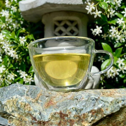 Sencha Fuji Steeped in glass tea cup on a rock with flowers.