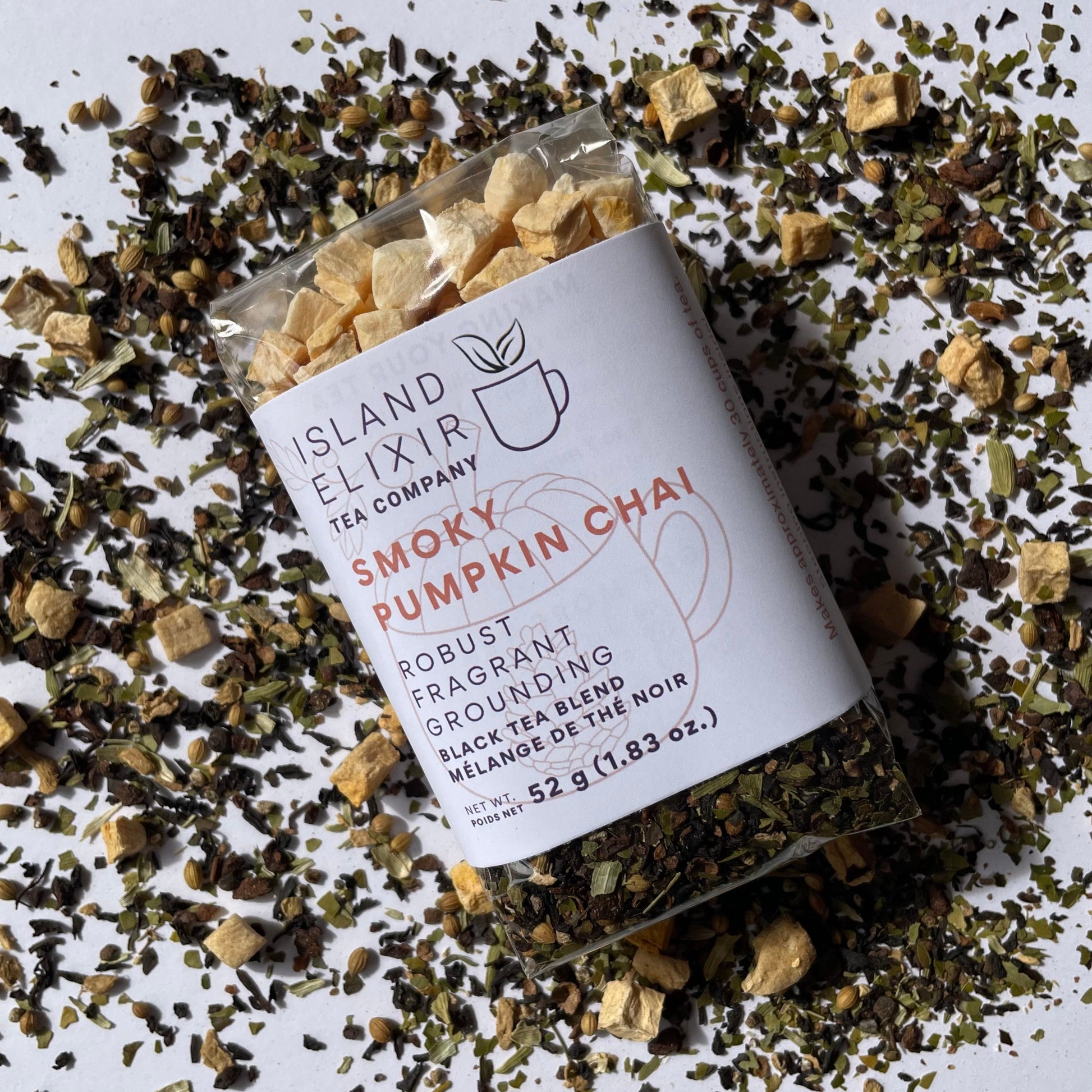 Island Elixir Smoky Pumpkin Chai tea 'Essential' size package surrounded by loose tea leaves on a white background