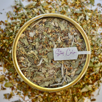 The Legends Herbal Tea 30 cups of tea size gold finish tin sitting on loose tea that contains Milk thistle seed, Osmanthus, Dandelion root, Alfalfa, Sage, Rosemary.