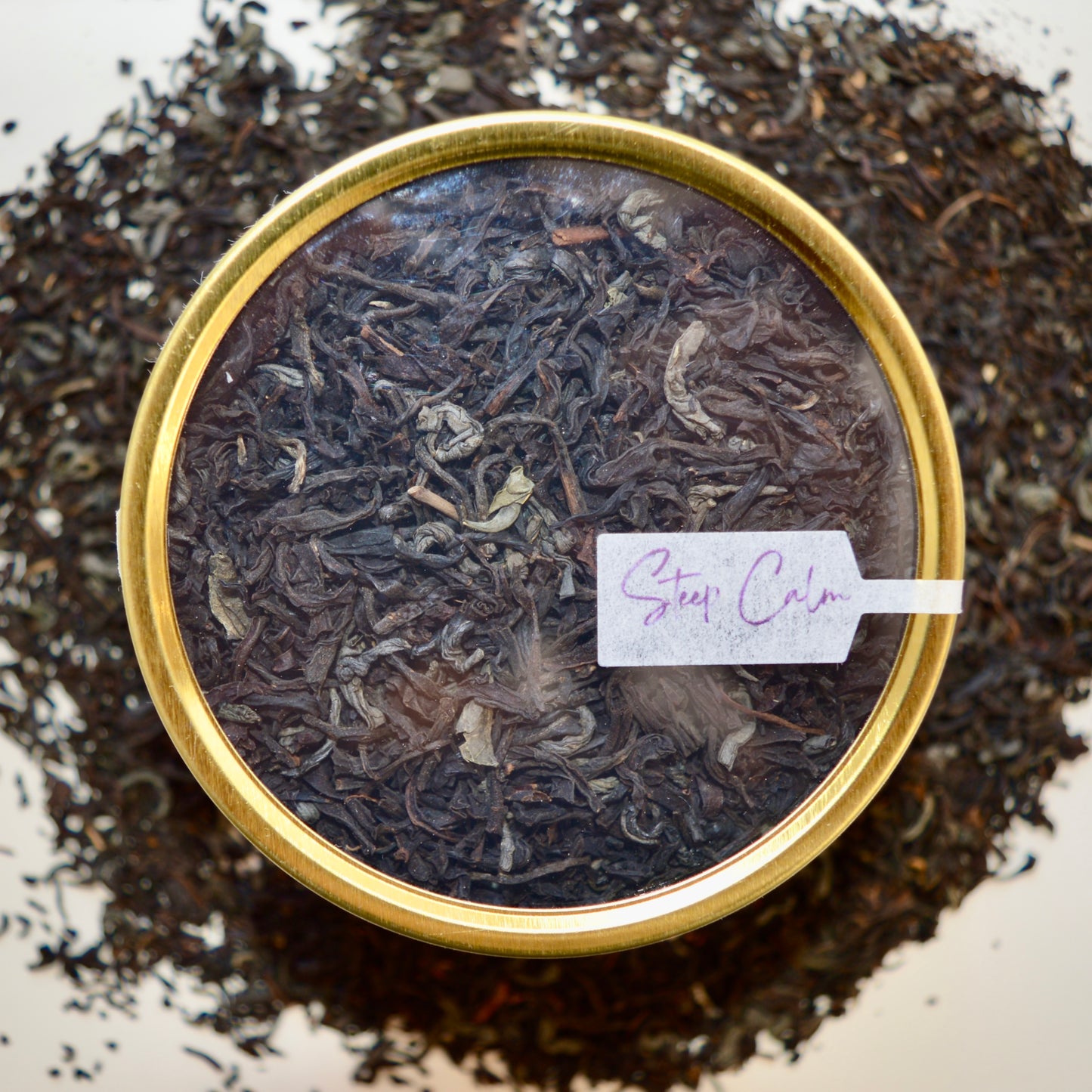 Top view Black Dragon Black Tea 30 cups of tea size gold finish tin sitting on loose leaf tea that contains Black tea*, Jasmine scented green tea*.