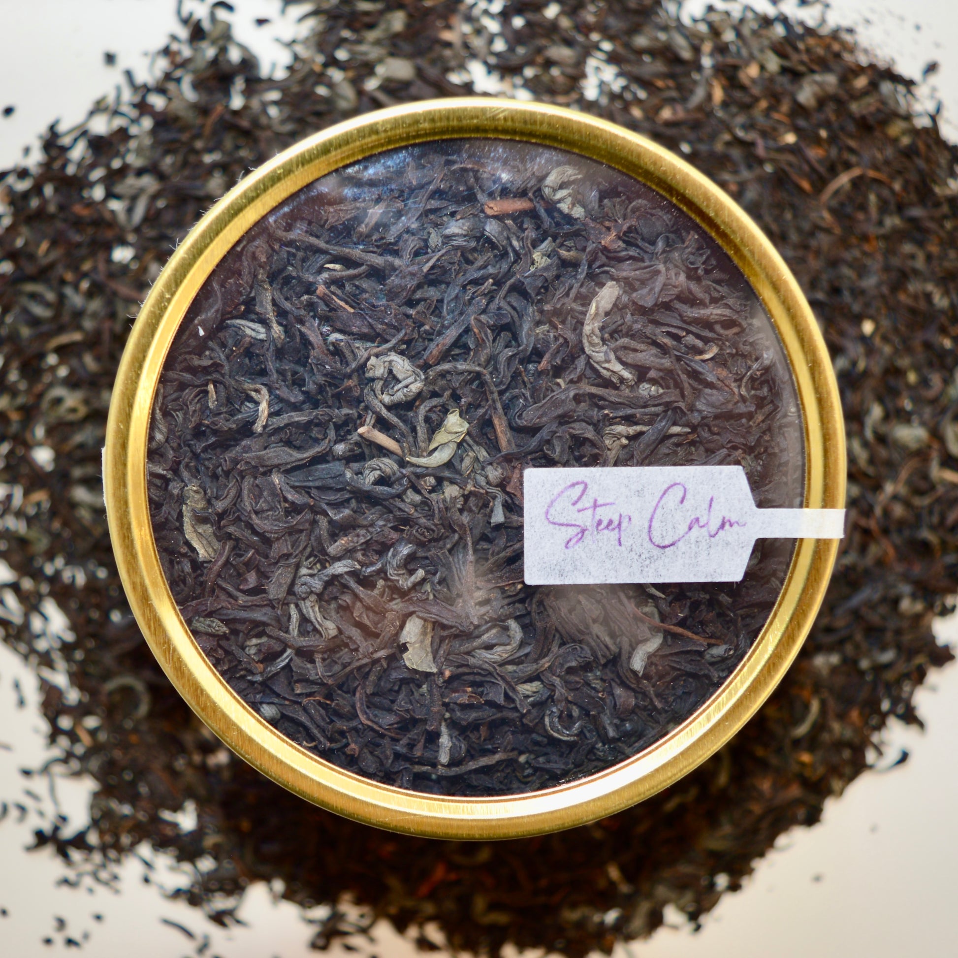 Top view Black Dragon Black Tea 30 cups of tea size gold finish tin sitting on loose leaf tea that contains Black tea*, Jasmine scented green tea*.