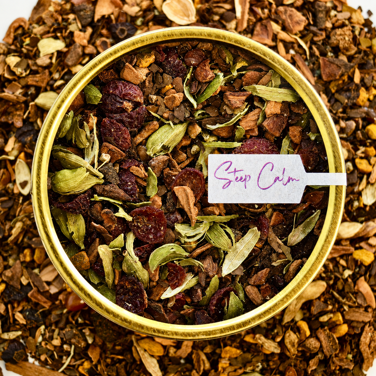 Top view sumitra's chai Herbal Tea 30 cups of tea size gold finish tin sitting on loose leaf tea that contains Cinnamon*, Cardamom*, Rose hip*, Star anise*, Turmeric*, Roasted maté*, Clove*, Ginger*