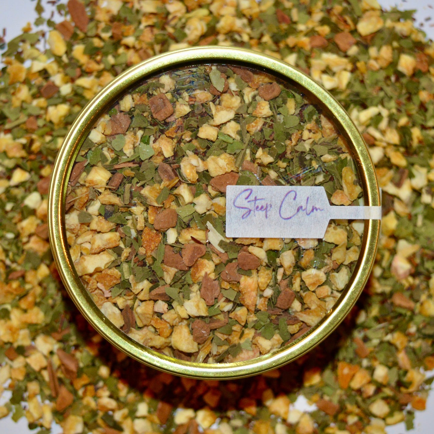 Vital Herbal Tea 30 cups of tea size gold finish tin sitting on loose leaf tea that contains orange pieces*, Yerba Maté*, Cinnamon (true)*, Rooibos*.